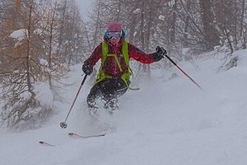 A person skiing down a snow covered slope with trees in the background