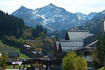image of some buildings with the green summer mountains surrounding them and some higher mountains in the background with snow on the tips