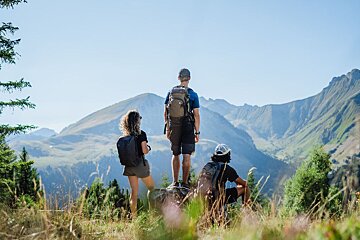 A man with a backpack is standing on a rocky trail in the mountains