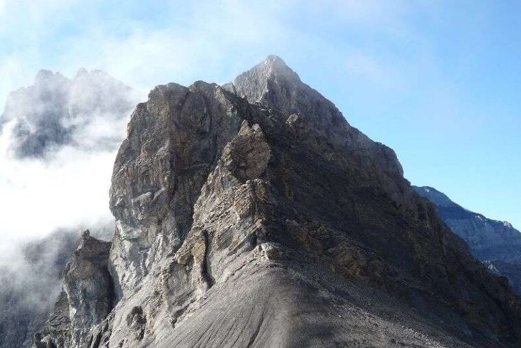 image of a rocky mountain peak with blue sky on the right and clouds on the left,