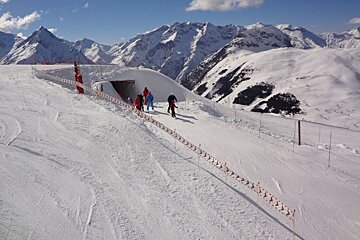 People skiing down a snowy slope with mountains in the background