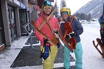 A woman in a pink jacket holds a pair of skis over her shoulder