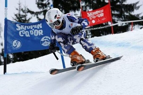 A person is skiing down a snow covered slope in front of a sign that says skoopen codor