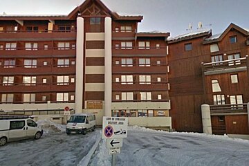 image of a large apartment block/building with cars parked out front and snow on the ground