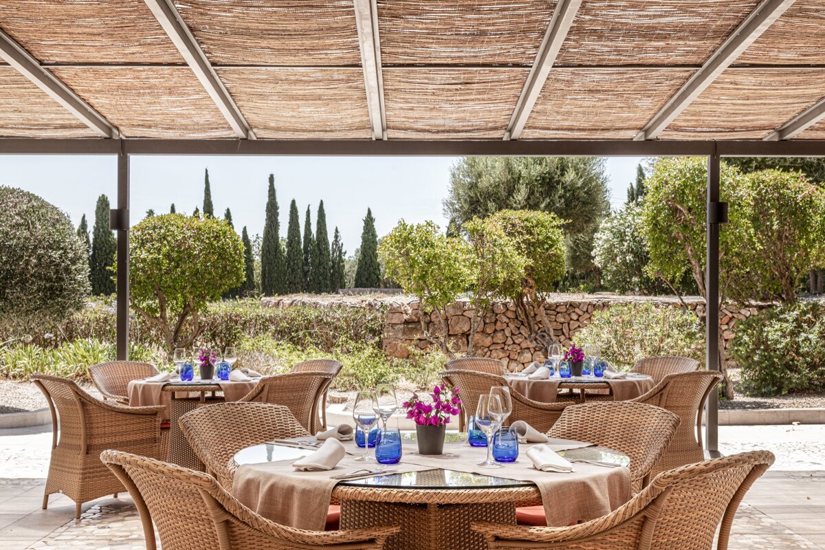 A restaurant with wicker chairs and tables with blue glasses on them