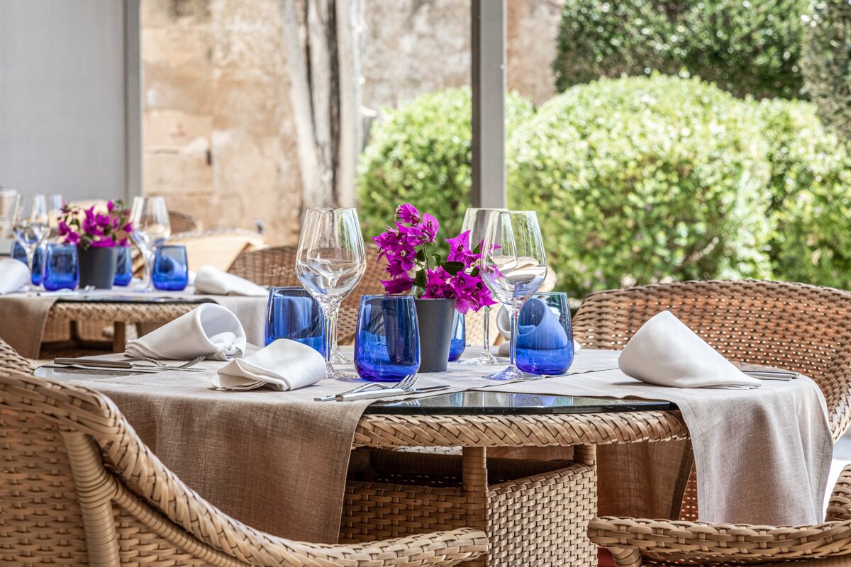 A wicker table with blue glasses and purple flowers on it