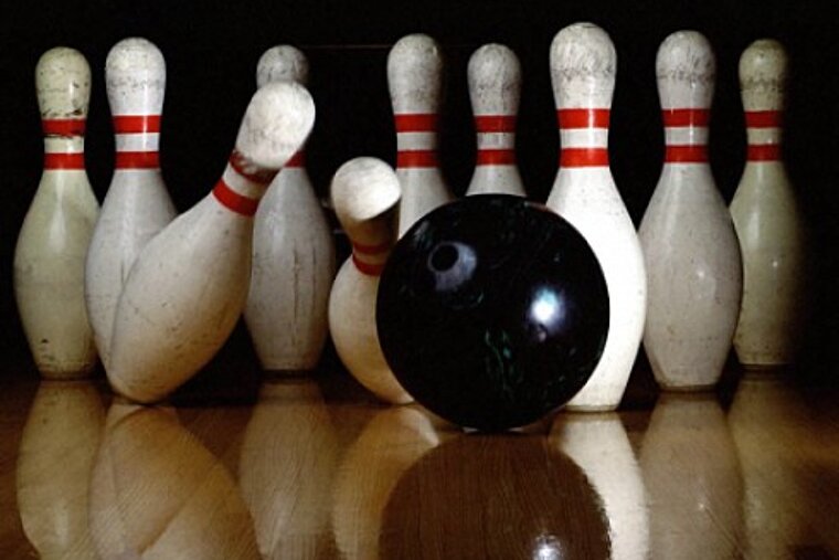 A bowling alley with white pins and a black ball