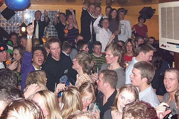 A crowd of people are gathered in a room with a pepsi machine in the corner