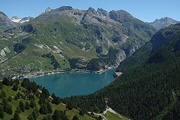 Image of a lake in the mountains with the tree lined green mountains and rocks surrounding the lake