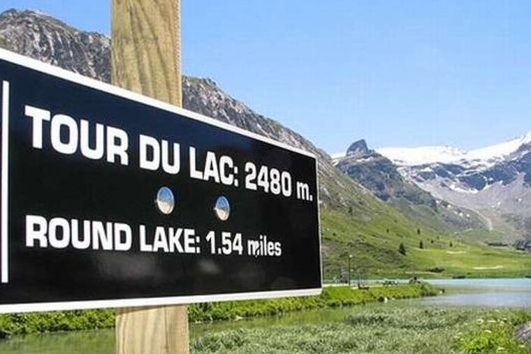 Image of sign and a lake and mountains covered in grass in the background