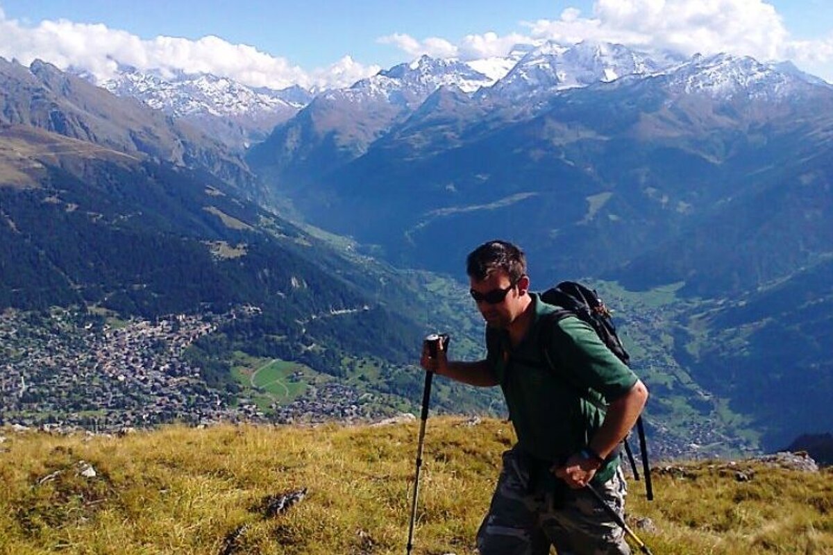 image of a man hiking on a mountain with the valley below him and snow covered mountain peaks in the distance