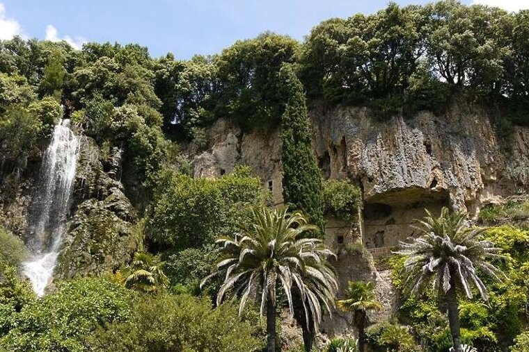 image of deep caves in cliffs with a waterfall and shrubbery on and surrounding the cave