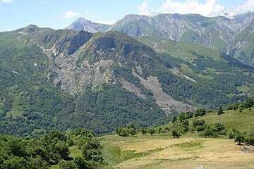 image of some mountains with green grass and trees on them and higher mountains in the distance, a meadow and trees on the mountain in the foreground