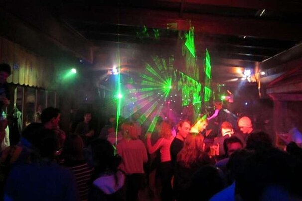 A crowd of people are dancing in a dark room with green and red lights