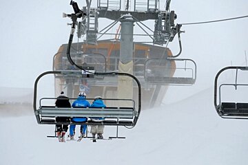 an image of skiers on a chairlift in wind
