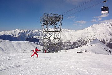A person skiing down a snowy slope with a ski lift in the background