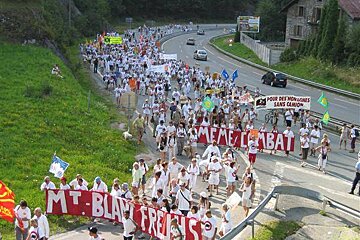 A large group of people march down a road holding signs that say mt. blair french