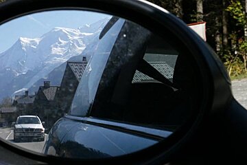 A car is reflected in a rear view mirror with mountains in the background