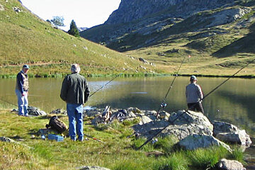 Three men are fishing in a lake with mountains in the background