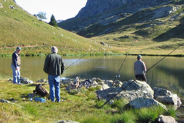 Three men are fishing in a lake with mountains in the background