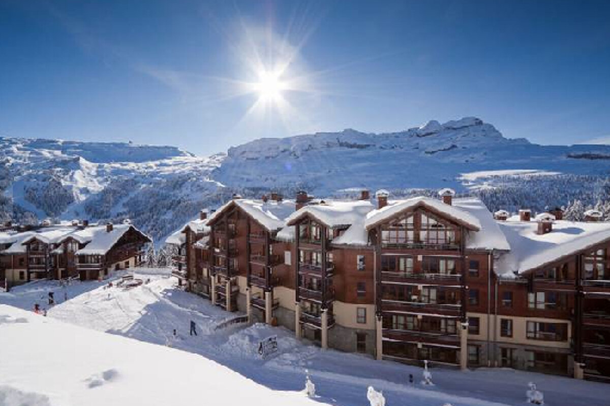 A ski resort with snow on the buildings and mountains in the background