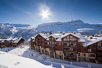 A ski resort with snow on the buildings and mountains in the background