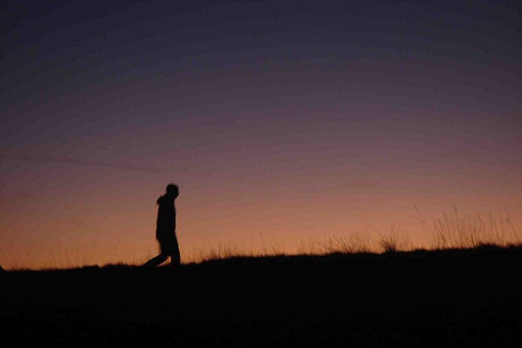 A silhouette of a person walking on a hill at sunset