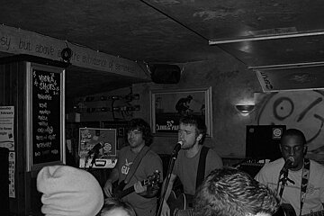 A black and white photo of a group of people playing guitars in front of a sign that says ' leningrad ' on it