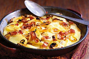 an image of an iron dish with tartiflette and a metal spoon