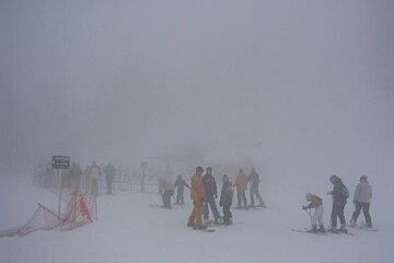 A group of people are skiing down a snow covered slope in the fog