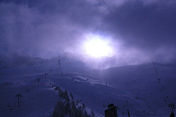 The sun is shining through the clouds over a snowy mountain