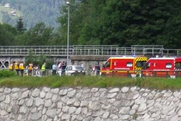 A group of people standing next to a stone wall and a red ambulance