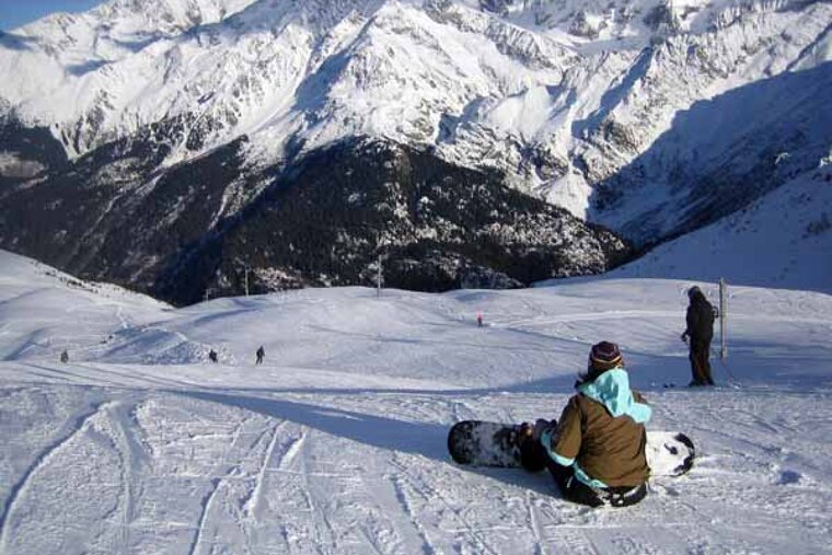 A person is sitting on a snowboard on top of a snow covered mountain