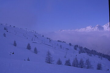 A snowy landscape with a blue sky and mountains in the background