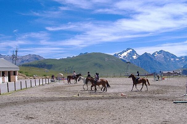 People riding horses in a dirt field with mountains in the background