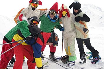 Six men on skis or boards in fancy dress