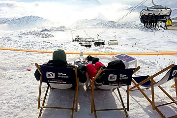 Couple in deck chairs looking out over chairlift and Alpe d'Huez