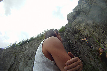 A man in a white tank top looks down at a woman climbing a rock wall