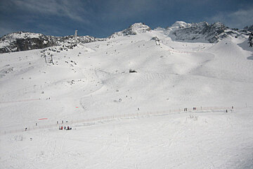 People skiing down a snow covered slope with mountains in the background