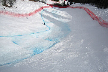 A person skiing down a snowy slope with a red fence