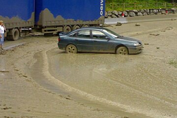 A car is driving through a muddy road next to a truck that says ogivit