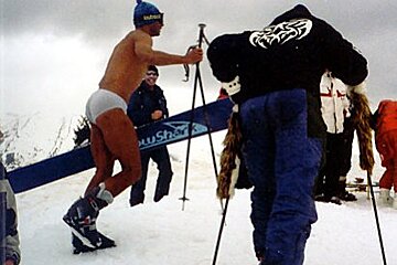 A man standing in the snow holding a blue ski that says ' pusher ' on it