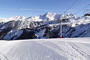 A ski lift going up a snowy slope with mountains in the background