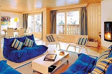 an image of a room with 2 blue sofas and patterned cushions with large windows behind