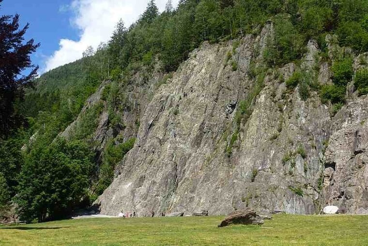 an image of a large crag with people climbing on it