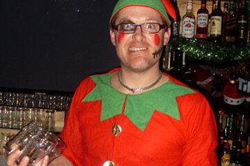 A man dressed in an elf costume holds a glass