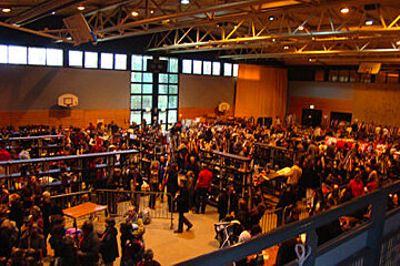 A large group of people are gathered in a gym with a basketball hoop in the background