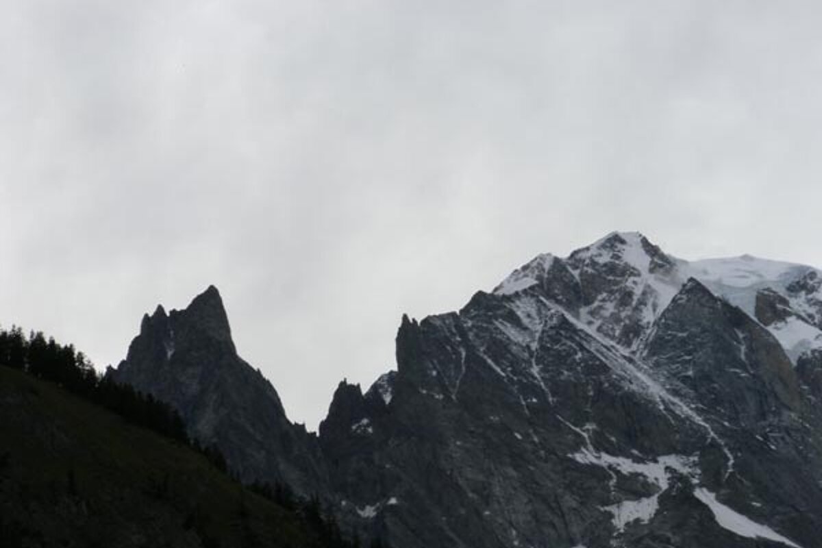 A mountain covered in snow and trees with a cloudy sky in the background