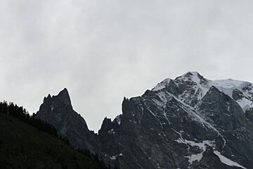 A mountain covered in snow and trees with a cloudy sky in the background