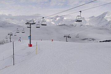 A ski lift going up a snow covered slope with mountains in the background